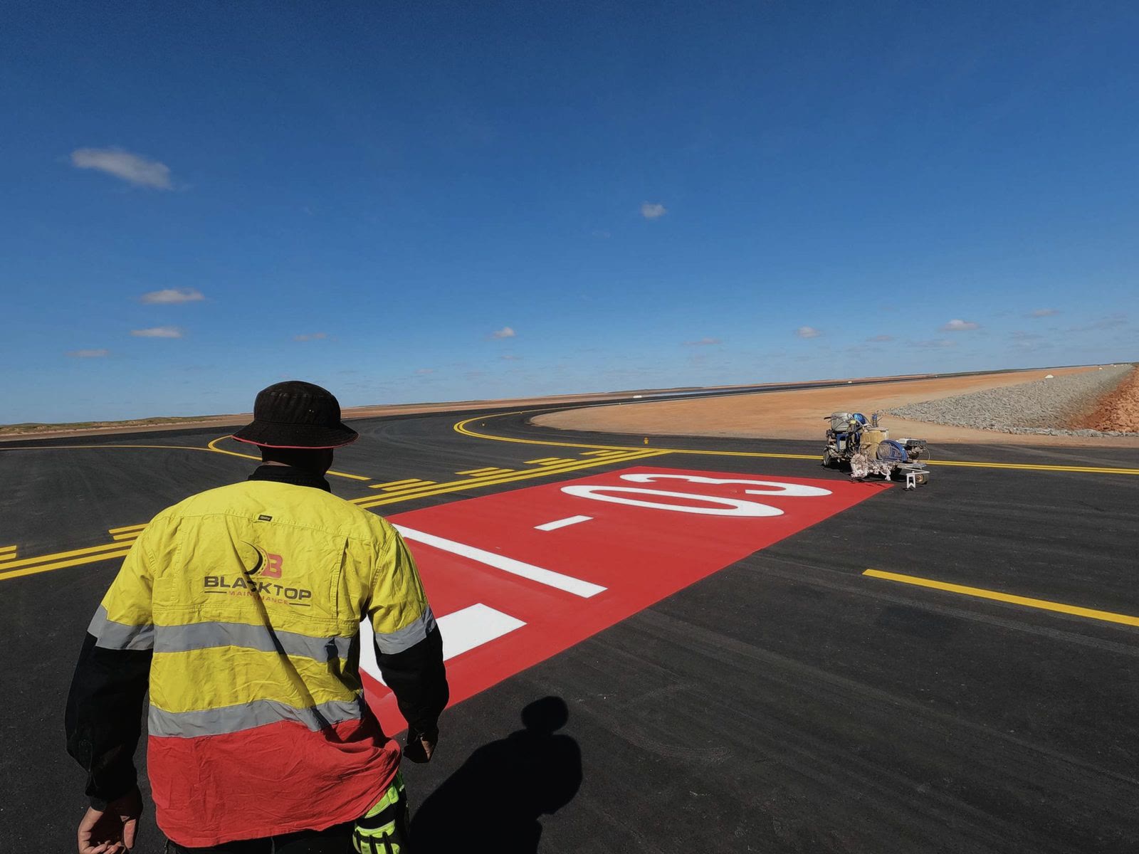 Blacktop Maintenance crew member overseeing freshly sprayed runway markings on an airport job